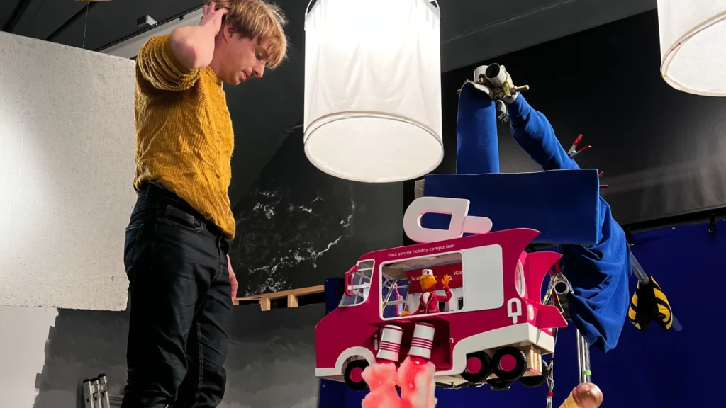 Stop-motion animator on set with a large, detailed pink ice cream truck puppet, demonstrating the intricate build and creative control in A+C Studios' animation production.
